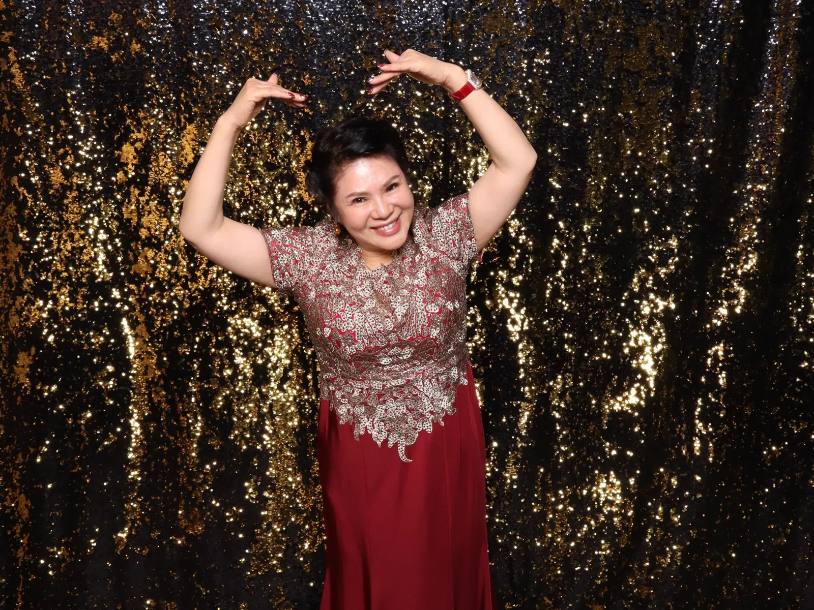 Celebrant in a red gown posing in front of a gold sequin backdrop